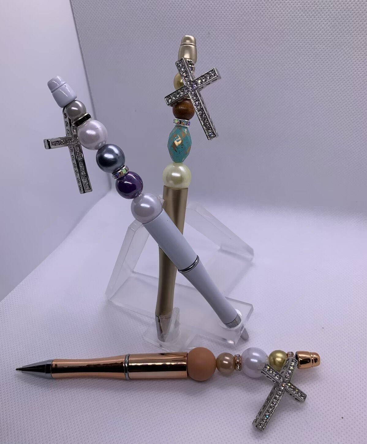 Elegant writing tools with bead and rhinestone detail, topped with a shimmering cross charm. Available in brown, white, gold, and mixed tones.